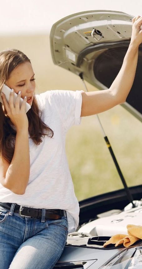 Driver on the phone beside a broken-down car with the bonnet open